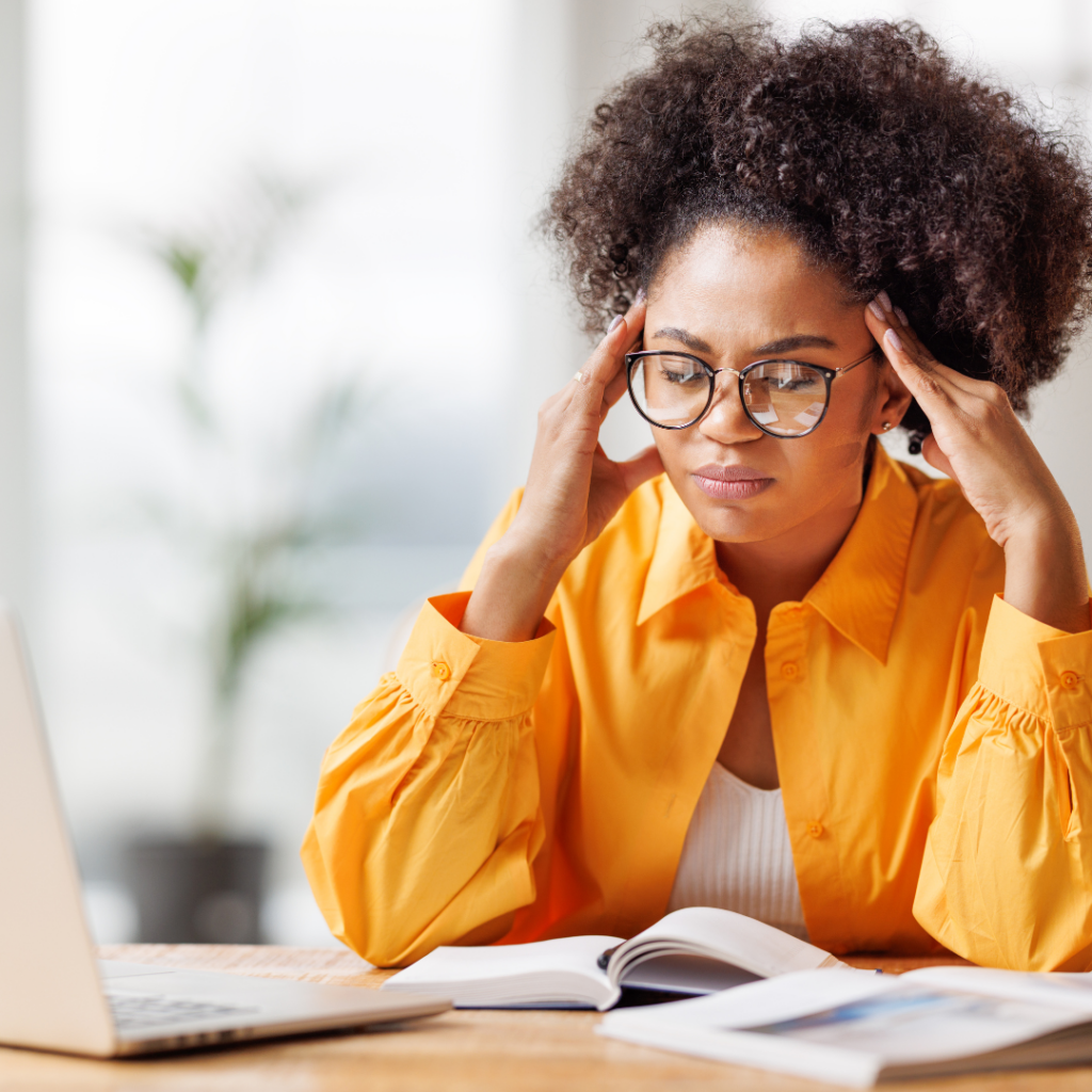 Frau sitzt am Schreibtisch und reibt sich die Schläfen weil sie Migräne hat.