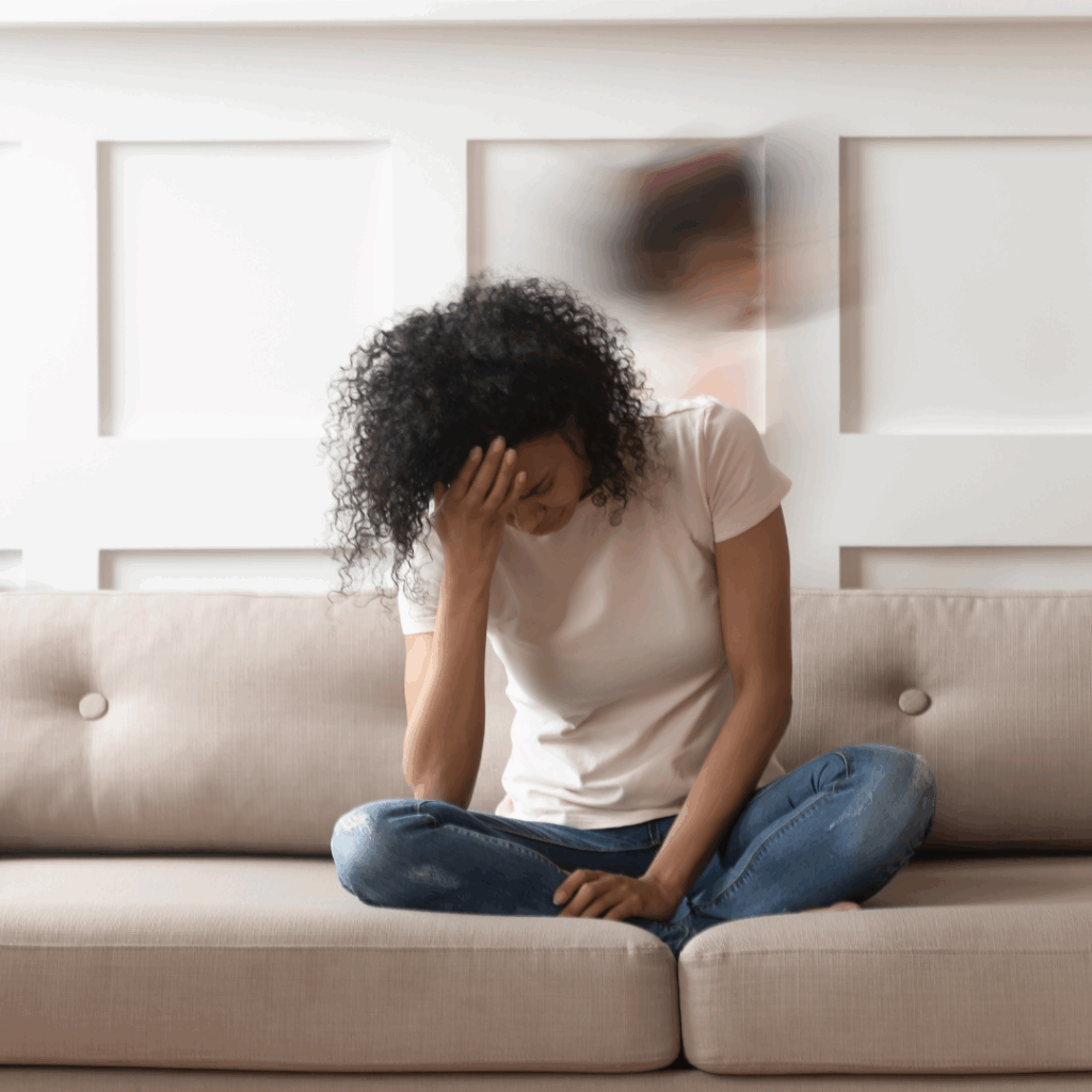 Erschöpfte Frau sitzt mit gesenktem Kopf auf dem Sofa, sichtbar gestresst – Symbolbild für mentale Belastung, Stress im Alltag und emotionale Überforderung.