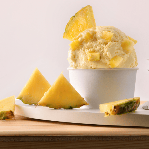Veganes Ananas-Kurkuma-Slush-Eis in einem weißen Becher, getoppt mit frischen Ananasstücken – zuckerfrei, hormonfreundlich und antientzündlich.