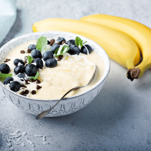 Vegane Blaubeer-Bananen-Nicecream in weißer Schale mit frischen Blaubeeren, Kokosraspeln und Minze – cremig, zuckerfrei & hormonfreundlich.