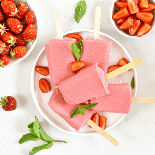 Selbstgemachtes Erdbeer-Kokos-Eis am Stiel – vegan, zuckerfrei, antientzündlich und hormonfreundlich, serviert mit frischen Erdbeeren und Minze.